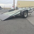 A trailer with a ramp on it is parked in the parking lot.