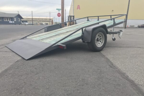 A trailer with a ramp on it is parked in the parking lot.